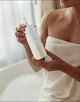 En kvinna står i morgonrock och håller i en BodyGliss Female Care Collection Care & Comfort Silicone 250 ml