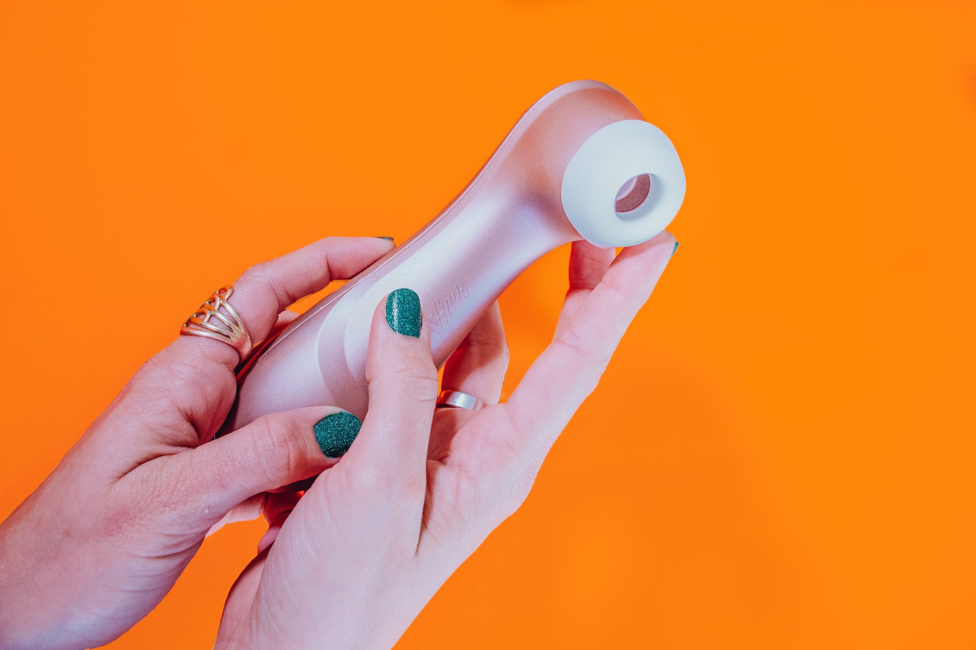 Kvinna håller i en Satisfyer Pro 2 Generation 2 mot orange bakgrund