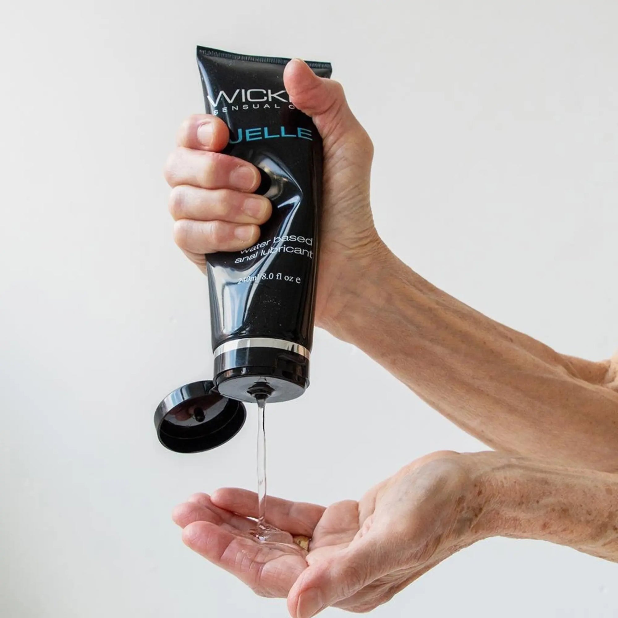 En hand häller Wicked Jelle Anal Vattenbaserat Glidmedel 240ml i sin andra hand
