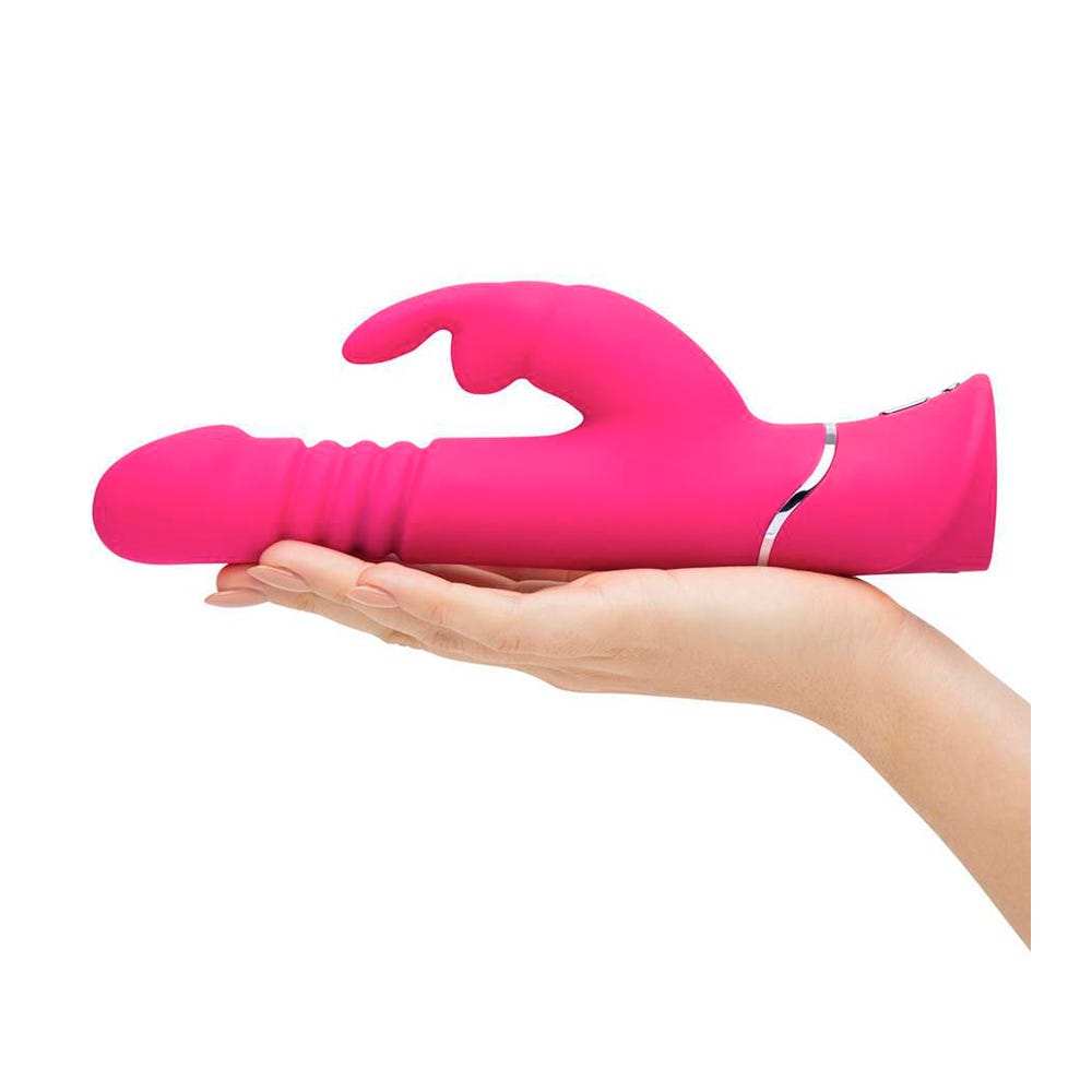 Kvinnlig hand som håller i Happy Rabbit Thrusting Realistic Rabbitvibrator mot vit bakgrund.