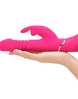 Kvinnlig hand som håller i Happy Rabbit Thrusting Realistic Rabbitvibrator mot vit bakgrund.