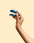 en hand som håller We-Vibe Chorus Cosmic Blue Samlagsvibrator mot gul bakgrund.