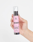 Hand som håller i Afrodita Silk Skin Body Lotion mot grå bakgrund.