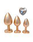 DreamToys Gleaming Love Gold Buttplug Set och ädelsten mot vit bakgrund.