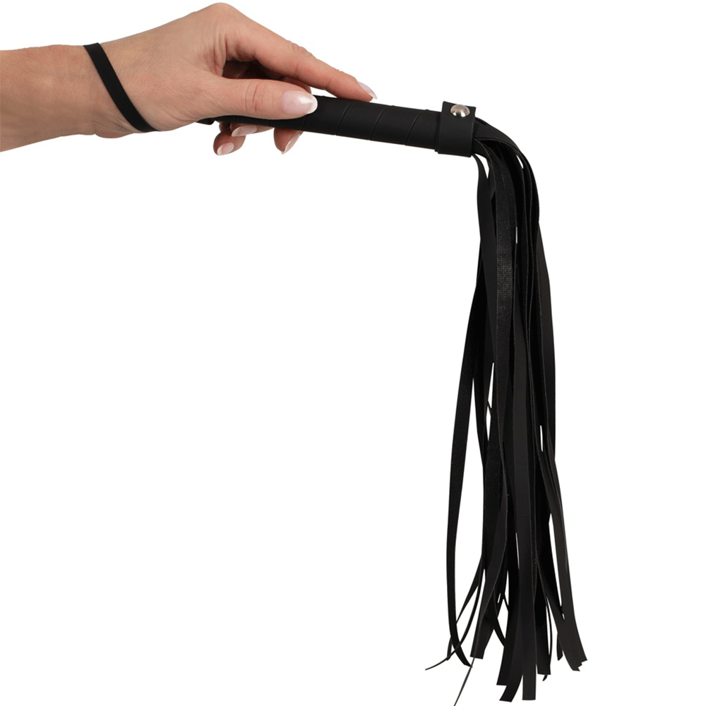 En hand som håller Magic Shiver Flogger och låter fransarna falla nedåt. Handen har ljus hud och välvårdade naglar.