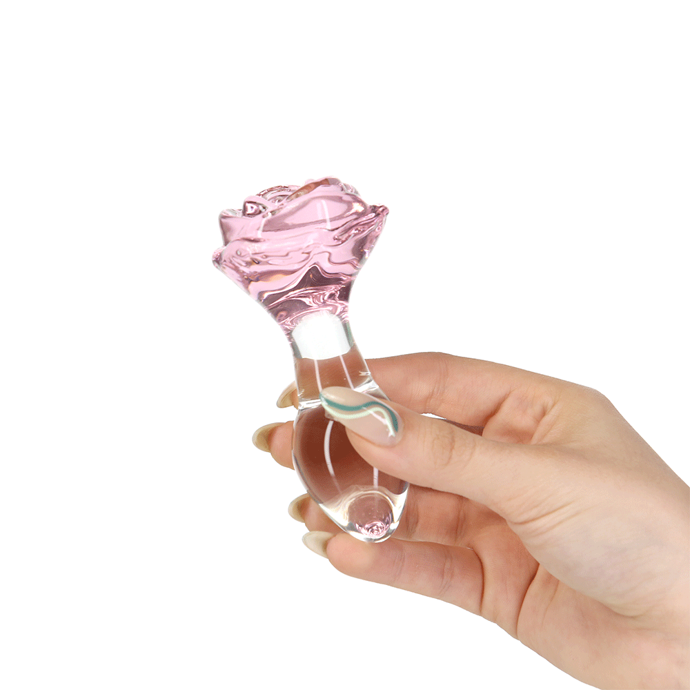 Hand som håller i Pillow Talk Rosy Luxurious Glass Anal Plug with Bonus Bullet mot vit bakgrund.