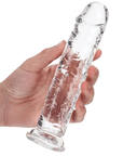 Hand med ljus hud som håller en RealRock Dildo with Suction Cup Clear 18cm. Mot vit bakgrund.