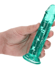 En hand med ljus hud som håller RealRock Dildo with Suction Cup Green 14,5cm mellan fingrarna. Vit bakgrund.