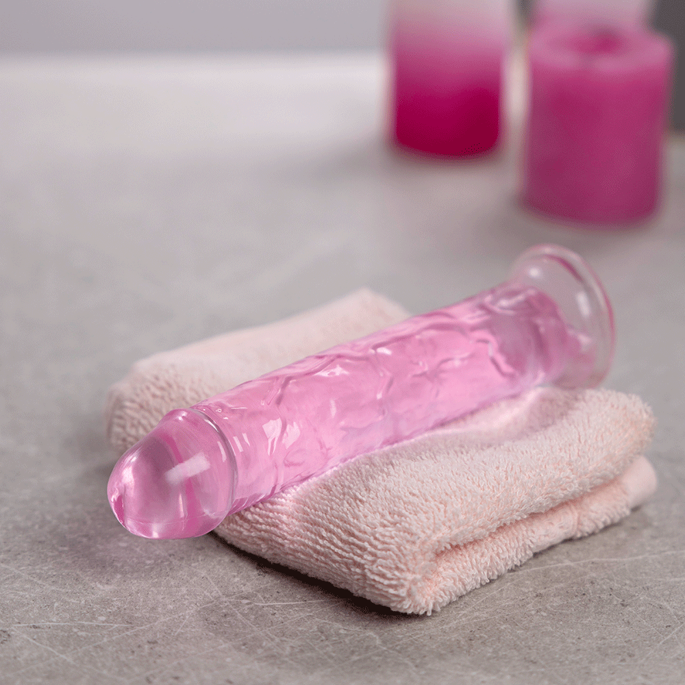 RealRock Dildo with Suction Cup Pink 18cm på en handduk och ljus i bakgrunden.