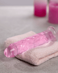 RealRock Dildo with Suction Cup Pink 18cm på en handduk och ljus i bakgrunden.