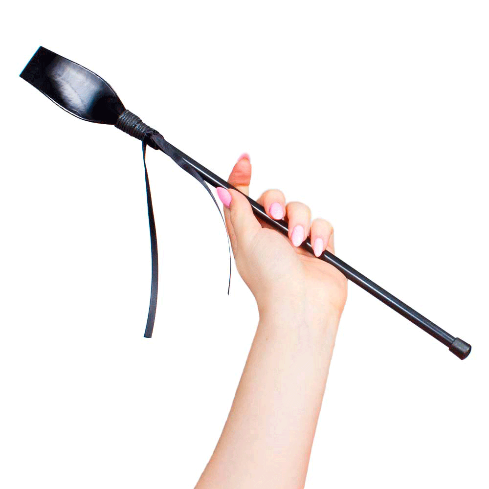 Hand med rosa naglar som håller i Secret Play Riding Crop Black mot vit bakgrund.