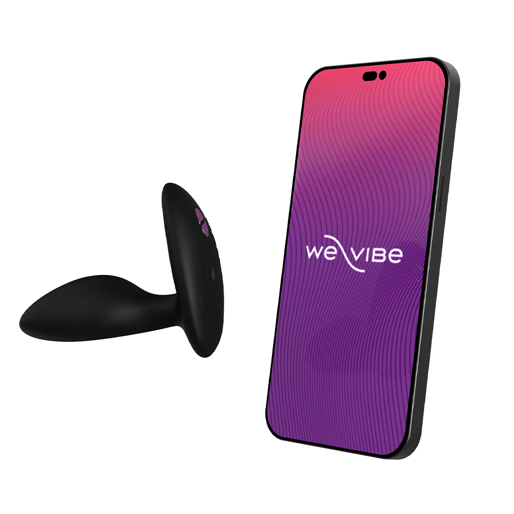 We-Vibe Ditto+ Satin Black bredvid en smartphone mot vit bakgrund.