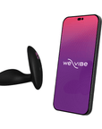 We-Vibe Ditto+ Satin Black bredvid en smartphone mot vit bakgrund.