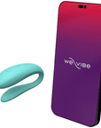 We-vibe Lite Aqua parvibrator bredvid en smartphone. På telefonens skärm syns logotyp. Vit bakgrund.