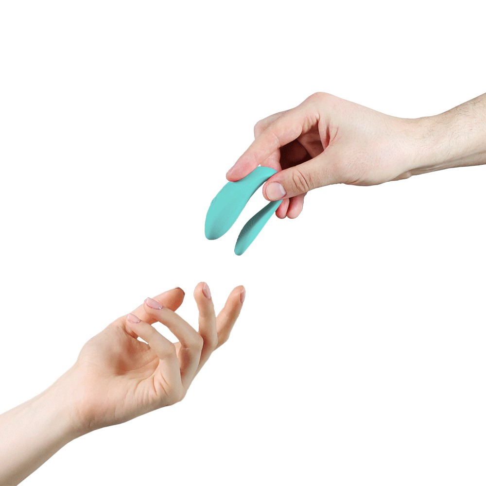 We-vibe Lite Aqua parvibrator i en hand som sträcker sig mot en annan hand. Vit bakgrund.