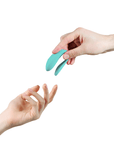 We-vibe Lite Aqua parvibrator i en hand som sträcker sig mot en annan hand. Vit bakgrund.