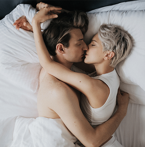par som kramas i en säng med vita lakan